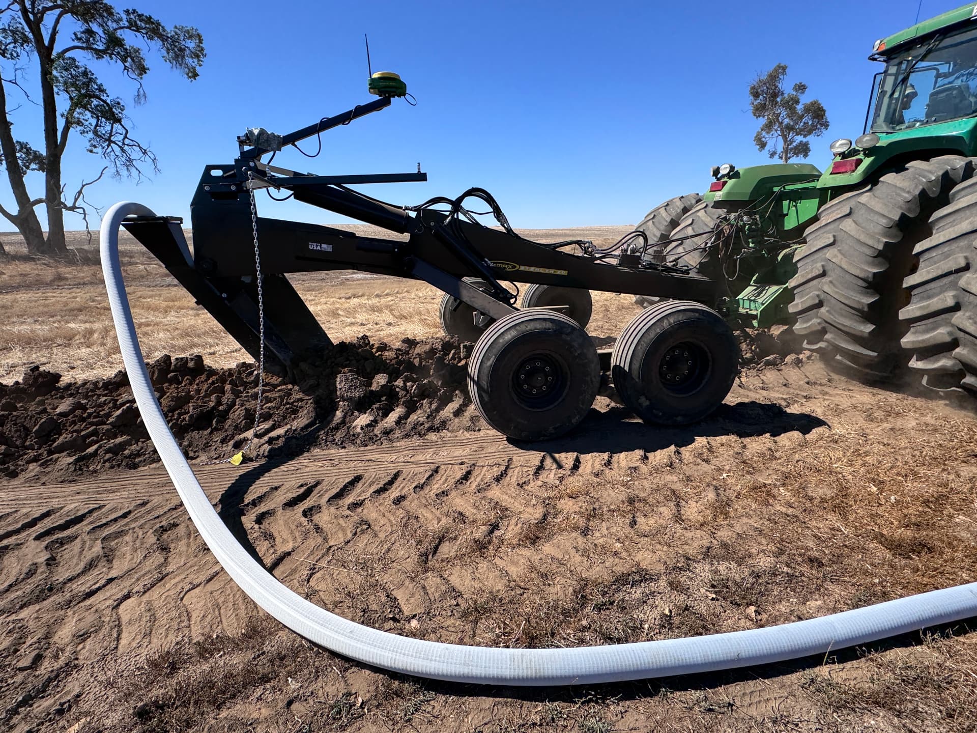 Soil-Max Stealth ZD tile plough hitched to a John Deere tractor laying white drainage pipe in a paddock